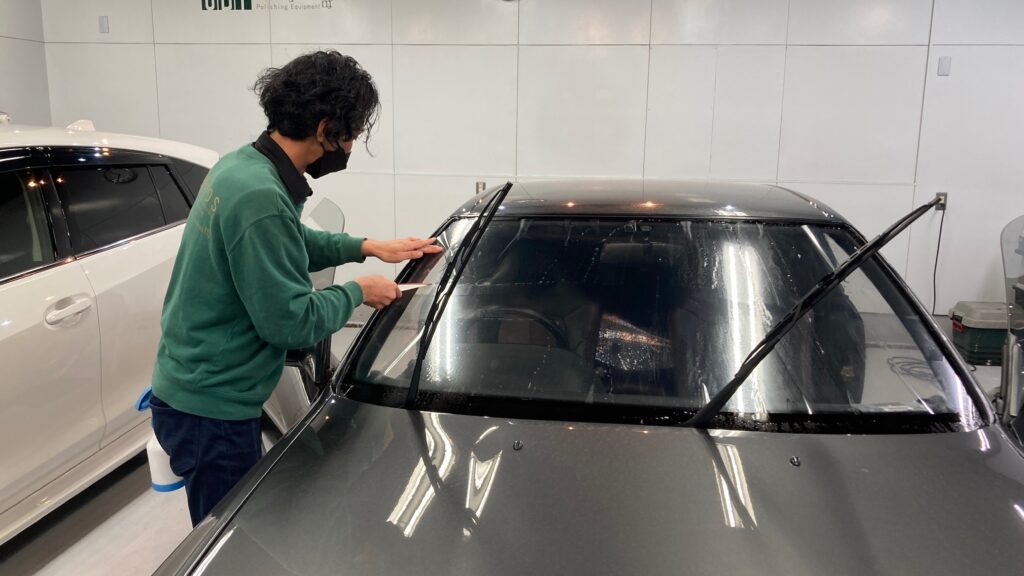 日産・GTR32カーフィルム施工工程：フロントガラスのフィルムを貼り付け、ヘラで伸ばしている様子