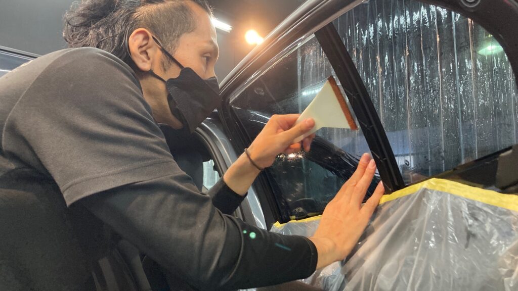 BMW・１シリーズ：カーフィルム施工：施工工程：リアドアガラスに貼るフィルムをヘラで伸ばしている様子