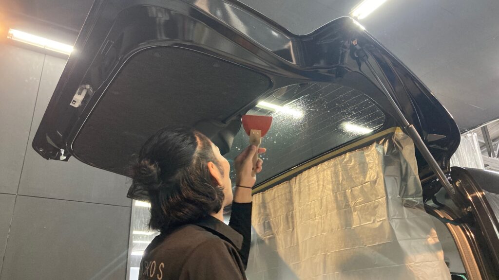 スズキ・ハスラーのカーフィルム施工：施工工程：リアガラスに貼ったフィルムをヘラで伸ばしている様子